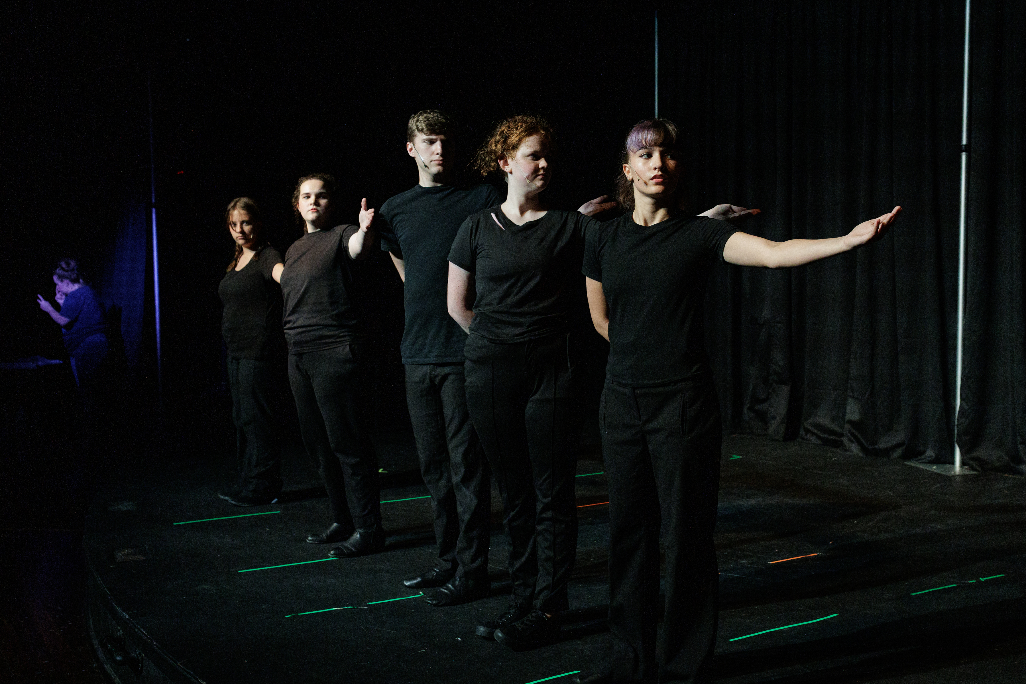 Black-clad performers form a diagonal line with arms extended in Two Part Tragedy.