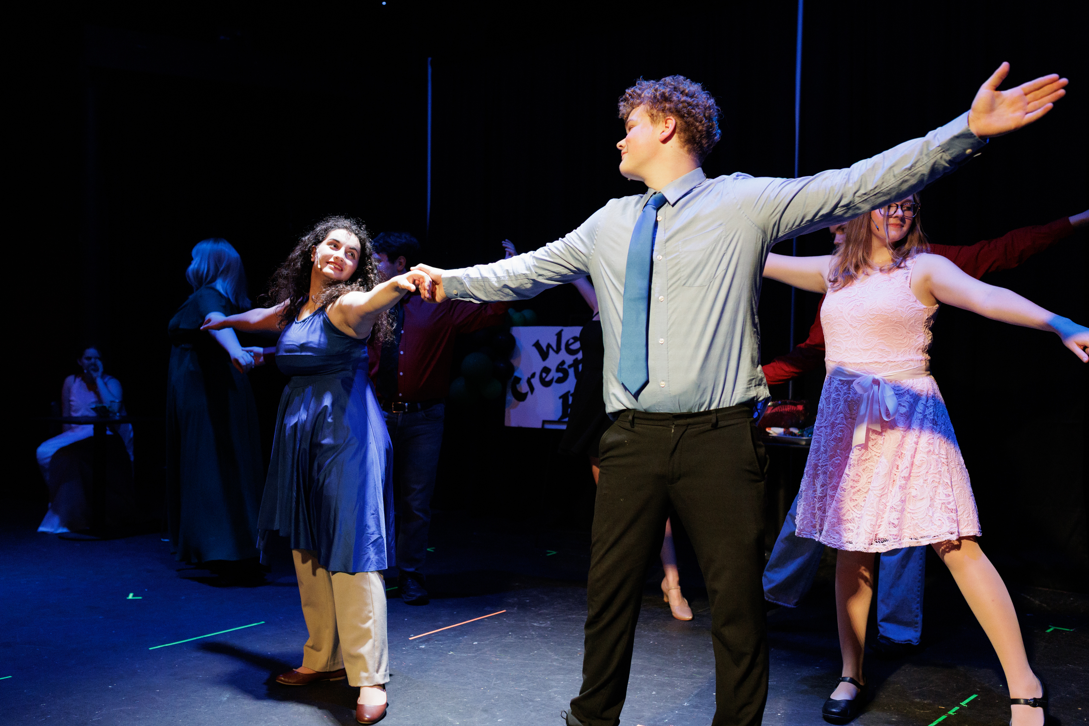 A performer in a shirt and tie extends an arm while holding a blue-dressed partner's hand in Two Part Tragedy.