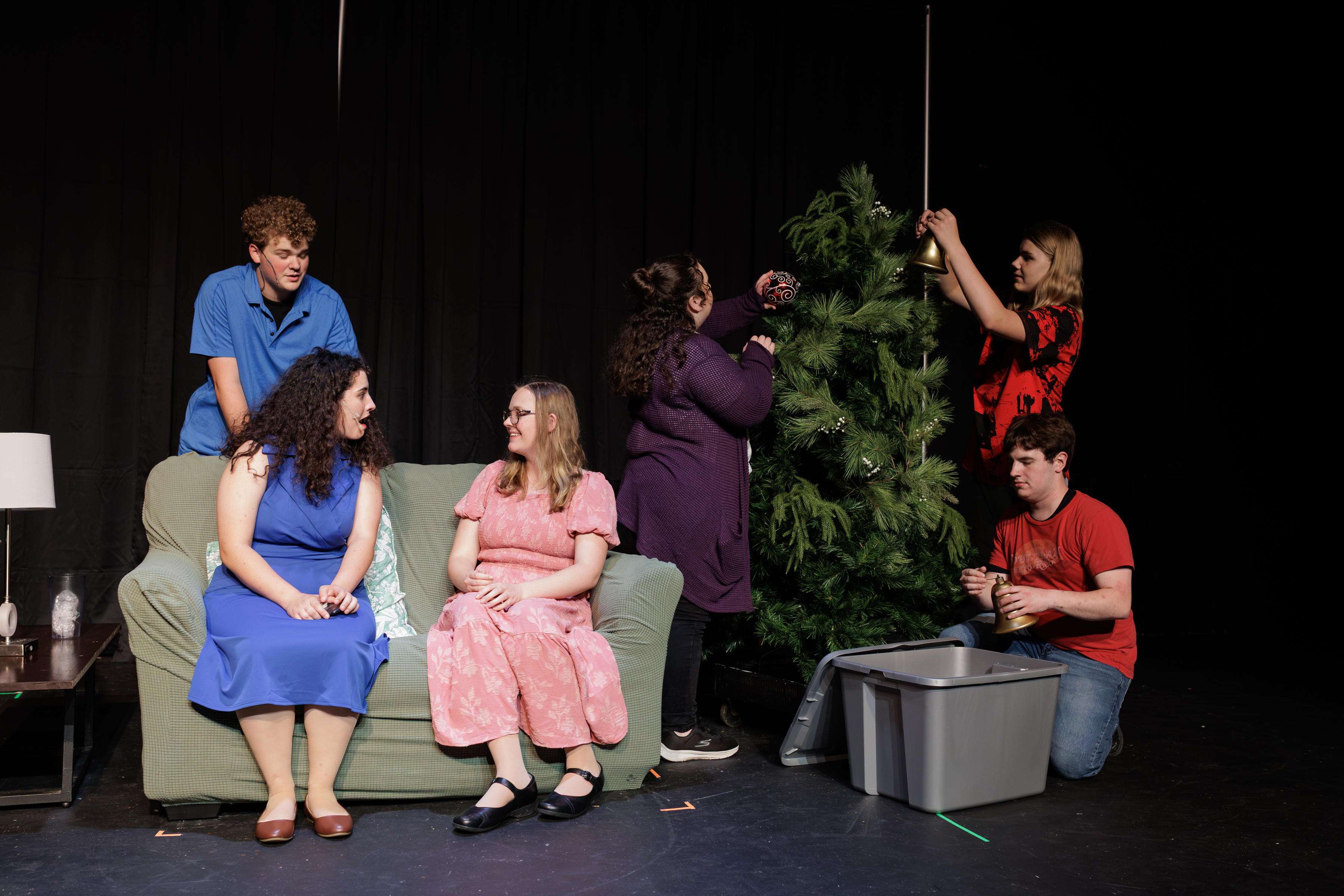 Performers decorate a tree while two others sit on a green sofa in Two Part Tragedy.