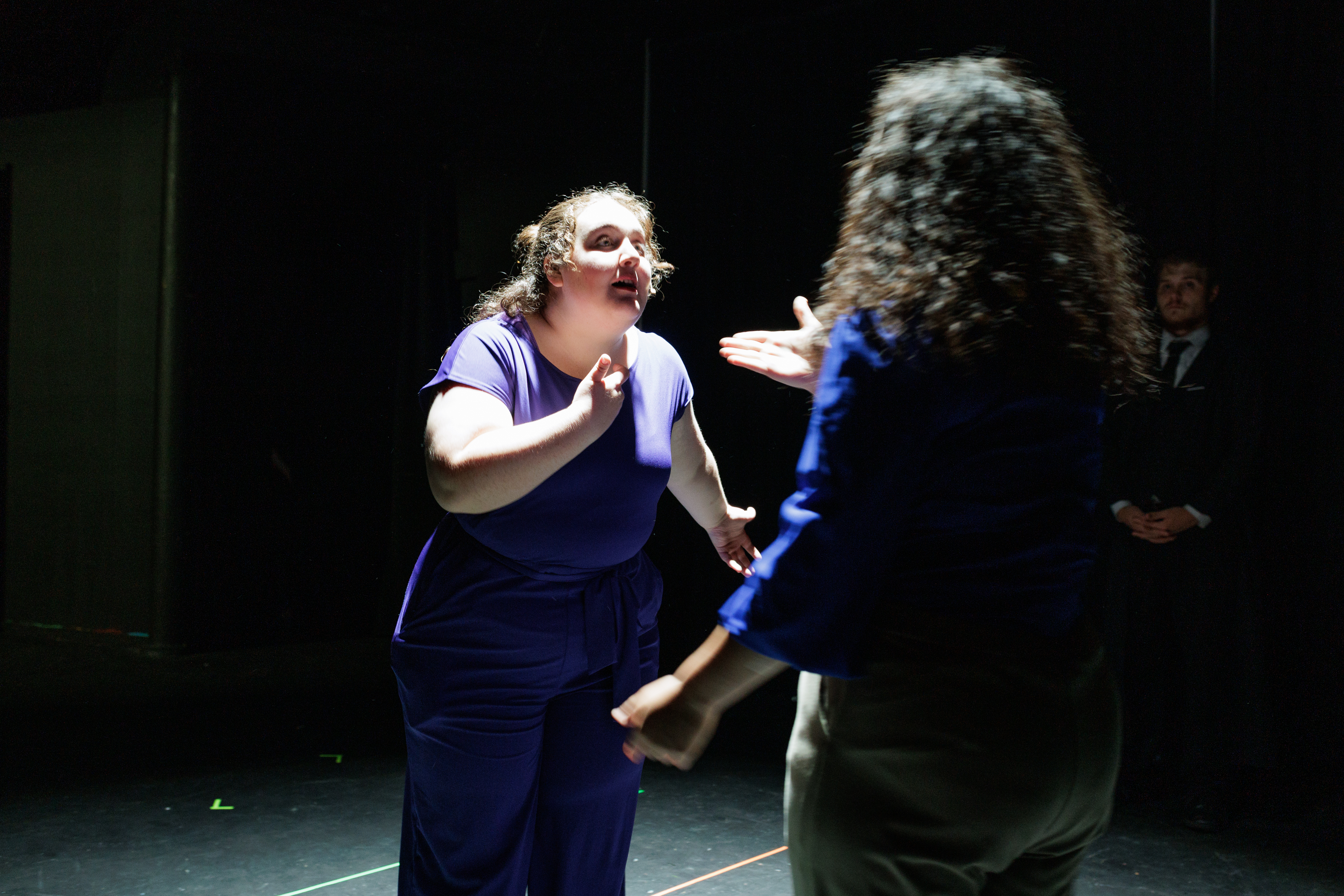 Two performers in blue and purple gesture face to face onstage in Two Part Tragedy.